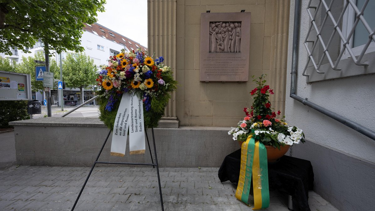 Gedenktafel am Asperger Bahnhof, davor ein Kranz und ein Blumengesteck